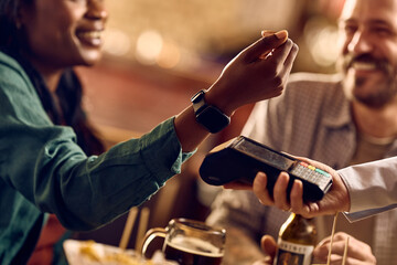 Close up of black woman paying contactless with smart watch in bar.