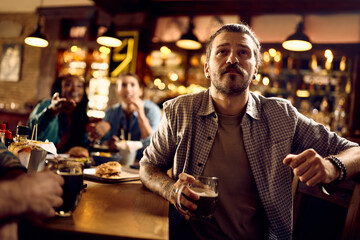 Young man watching sports match with his friends while drinking beer in pub.