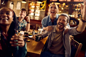 Cheerful friends celebrating victory of their favorite team while watching match in pub.