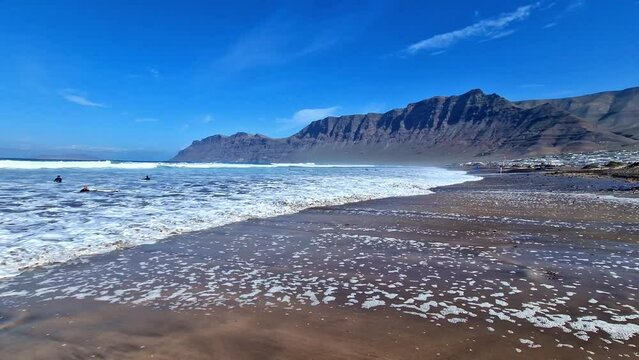 Caleta de Famara Lanzarote Canary Islands Spain 4K. Scenic view of sandy beach with crashing ocean waves and Famara cliff background. Popular surfing destination b roll footage travel stock video