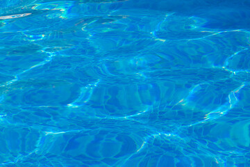 superficie del agua turquesa de una piscina con los reflejos del sol sobre el agua azul