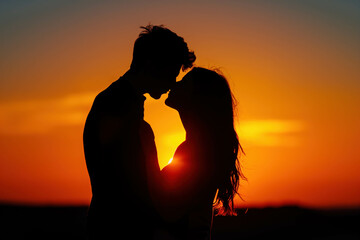 Silhouette of a young couple in love face to face against the background of the orange sky during sunset.