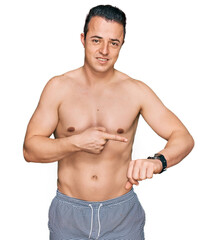 Obraz premium Handsome young man wearing swimwear shirtless in hurry pointing to watch time, impatience, upset and angry for deadline delay