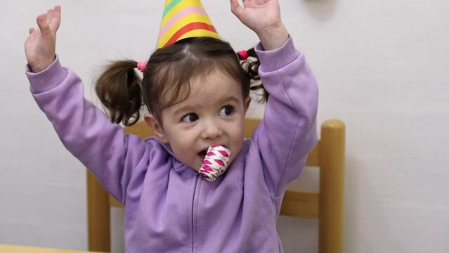 A little girl blows a whistle on a birthday party.