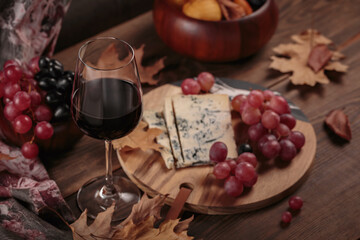 Glass of red wine served with blue cheese on dark wooden background. Autumn picnic with wine and cheese platter, fruits and dry leaves in rustic style