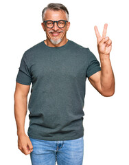 Naklejka premium Middle age grey-haired man wearing casual clothes and glasses smiling with happy face winking at the camera doing victory sign. number two.