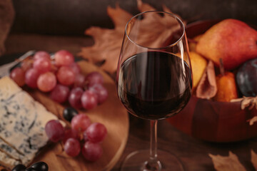 Glass of red wine served with blue cheese on dark wooden background. Autumn picnic with wine and cheese platter, fruits and dry leaves in rustic style - obrazy, fototapety, plakaty