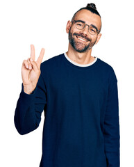 Fototapeta premium Hispanic man with ponytail wearing casual sweater and glasses showing and pointing up with fingers number two while smiling confident and happy.
