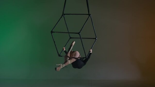Portrait of female acrobat on colorful background. Woman aerialist dancer in split on high heels in the air on cube with ropes.
