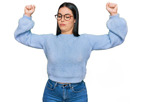 Young hispanic woman wearing casual clothes and glasses showing arms muscles smiling proud. fitness concept.