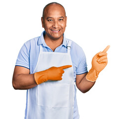 Hispanic middle age man wearing cleaner apron and gloves smiling and looking at the camera pointing...