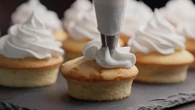 Decorating cupcake with white cream using cooking bag. Homemade bakery concept. Confectioner making vanilla cupcakes for party. Italian meringue. Closeup in 4K, UHD
