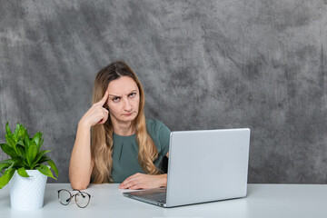 Trendy Blond Girl Showing Various Poses Near Laptop and Green Flower in Gray Dress