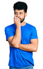 Young arab man with beard wearing casual blue t shirt looking stressed and nervous with hands on mouth biting nails. anxiety problem.