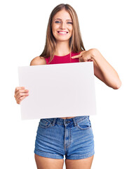 Young beautiful blonde woman holding blank empty banner pointing finger to one self smiling happy and proud