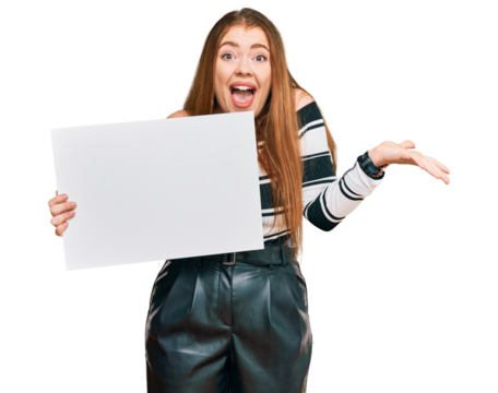 Young beautiful redhead woman holding blank empty banner celebrating victory with happy smile and winner expression with raised hands