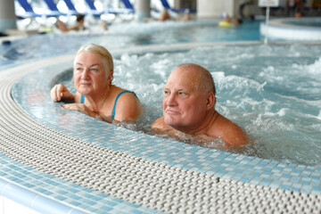Happy elderly couple enjoying hydromassage in the swimming pool at the spa.