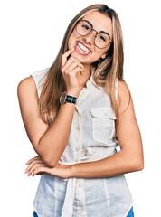 Hispanic young woman wearing casual white shirt looking confident at the camera with smile with crossed arms and hand raised on chin. thinking positive.