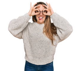 Young blonde woman wearing casual sweater and glasses doing ok gesture like binoculars sticking tongue out, eyes looking through fingers. crazy expression.