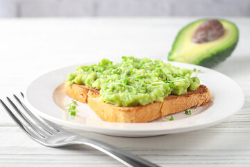 A slice of fresh bread on a plate with avocado on a background of light wooden boards