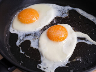 Two fried eggs seasoned with sea salt in a frying pan. Close up.