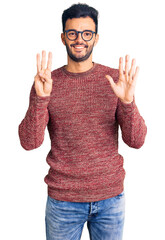 Naklejka premium Young handsome hispanic man wearing winter sweater and glasses showing and pointing up with fingers number eight while smiling confident and happy.