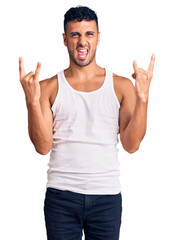 Young hispanic man wearing casual clothes shouting with crazy expression doing rock symbol with hands up. music star. heavy concept.