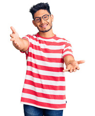 Naklejka premium Handsome latin american young man wearing casual clothes and glasses looking at the camera smiling with open arms for hug. cheerful expression embracing happiness.