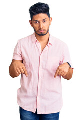 Handsome latin american young man wearing casual summer shirt pointing down looking sad and upset,...