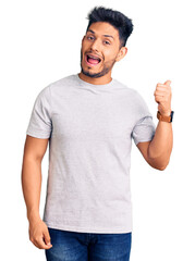 Handsome latin american young man wearing casual tshirt smiling with happy face looking and pointing to the side with thumb up.