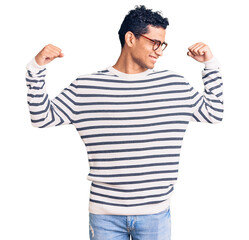 Naklejka premium Hispanic handsome young man wearing casual clothes and glasses showing arms muscles smiling proud. fitness concept.