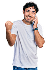 Hispanic young man with beard having conversation talking on the smartphone screaming proud, celebrating victory and success very excited with raised arm