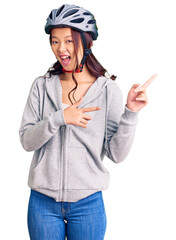 Young beautiful chinese girl wearing bike helmet smiling and looking at the camera pointing with two hands and fingers to the side.