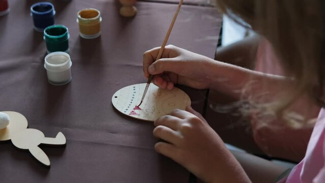 Close-up of little girl making Easter decoration in the kitchen, painting wooden egg 