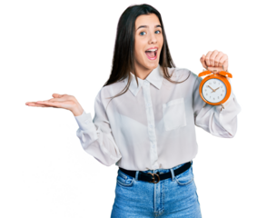 Young brunette teenager holding alarm clock celebrating achievement with happy smile and winner expression with raised hand