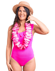 Young beautiful brunette woman wearing swimwear and hawaiian lei smiling doing phone gesture with...