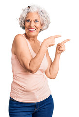 Senior grey-haired woman wearing casual clothes smiling and looking at the camera pointing with two hands and fingers to the side.