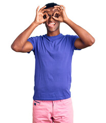 African handsome man wearing casual clothes and glasses doing ok gesture like binoculars sticking tongue out, eyes looking through fingers. crazy expression.