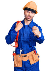 Young hispanic man wearing elecrician uniform holding cable annoyed and frustrated shouting with anger, yelling crazy with anger and hand raised