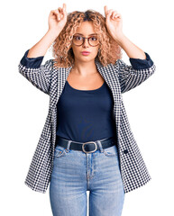 Young blonde woman with curly hair wearing business jacket and glasses doing funny gesture with...
