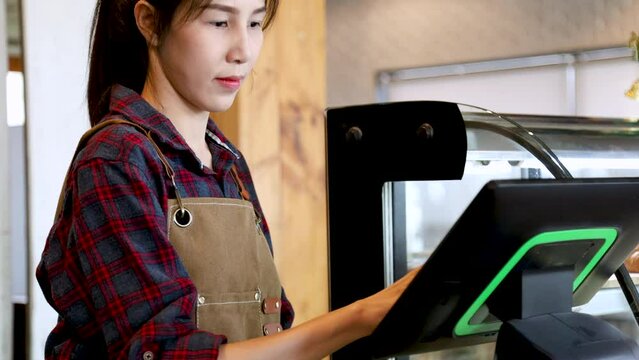 Closeup Asian cafe small business owner female taking customer order by modern POS purchasing order system machine making selling transaction standing in counter, barista waitress worker happy smiling