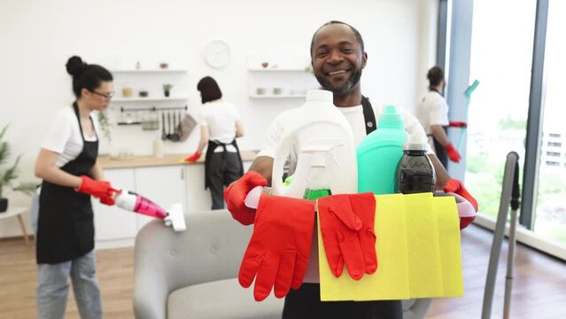 Portrait of young African American man professional cleaning worker holding a bucket for washing with detergents on bright kitchen studio background, copy space.