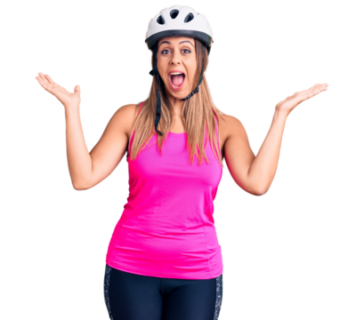 Young beautiful woman wearing bike helmet celebrating victory with happy smile and winner expression with raised hands - Powered by Adobe