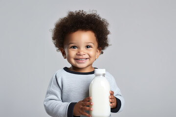 Little african american baby boy drinks milk from a bottle on grey background - Powered by Adobe