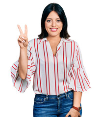 Young hispanic girl wearing casual clothes smiling looking to the camera showing fingers doing...
