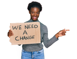Young african american girl holding we need a change banner smiling happy pointing with hand and finger to the side