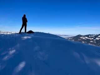 Silhouette of man standing on snow peak looking down on Rhine Valley and Lake of Constance, Vorarlberg, Austria.