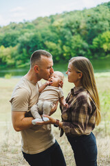 Happy family couple with little newborn son in nature. Happy young mother and father with a child on a walk in the forest. The concept of a happy married couple with a child