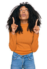 Young african american girl wearing casual clothes amazed and surprised looking up and pointing with fingers and raised arms.