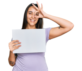 Young hispanic woman holding blank empty banner smiling happy doing ok sign with hand on eye looking through fingers